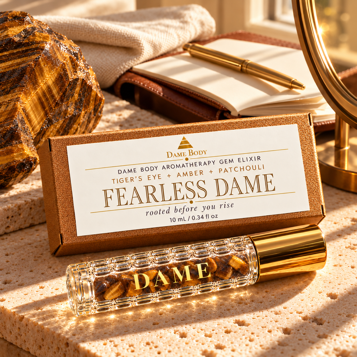 Fearless Dame roller and labeled kraft box beside a notebook, cream linen and raw Tiger&rsquo;s Eye in warm light.