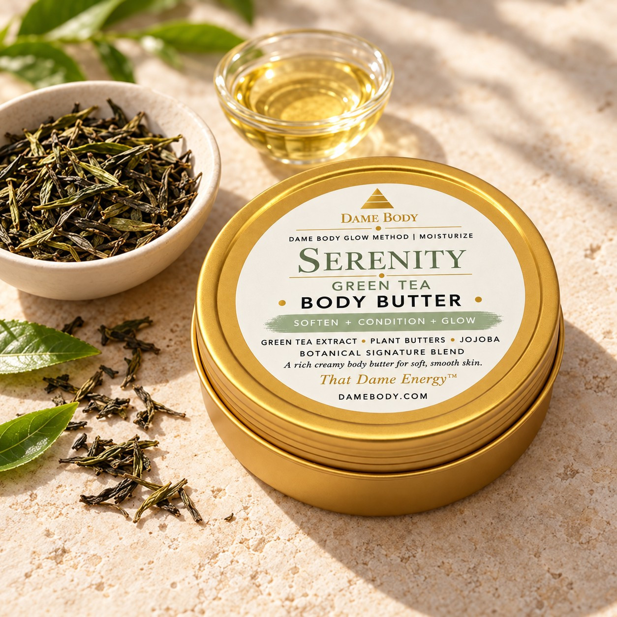 Current-label Serenity Green Tea 4oz Gold Tin Body Butter with green tea leaves and a bowl of golden oil, illustrating this blend&rsquo;s botanical story.