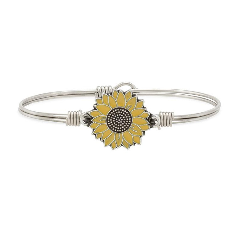 The Sunflower is the national flower of Ukraine and now more than ever, they represent solidarity + strength. With the tragic events happening in our world, we are here in full support of Ukraine and believe in the power of peace. This hopeful blossom is finished with yellow and brown enamel and radiant gold-tone touches.

We are donating 50% of proceeds from the Yellow Sunflower Bangle to Sunflower of Peace, a 501(c)(3) non-profit organization providing backpacks to Ukrainian soldiers, citizens and volunteers with crucial first aid supplies.

Easy hook and catch closure
Oval shape ensures proper fit
Silver tone finish
Includes an essence card
Made in the USA