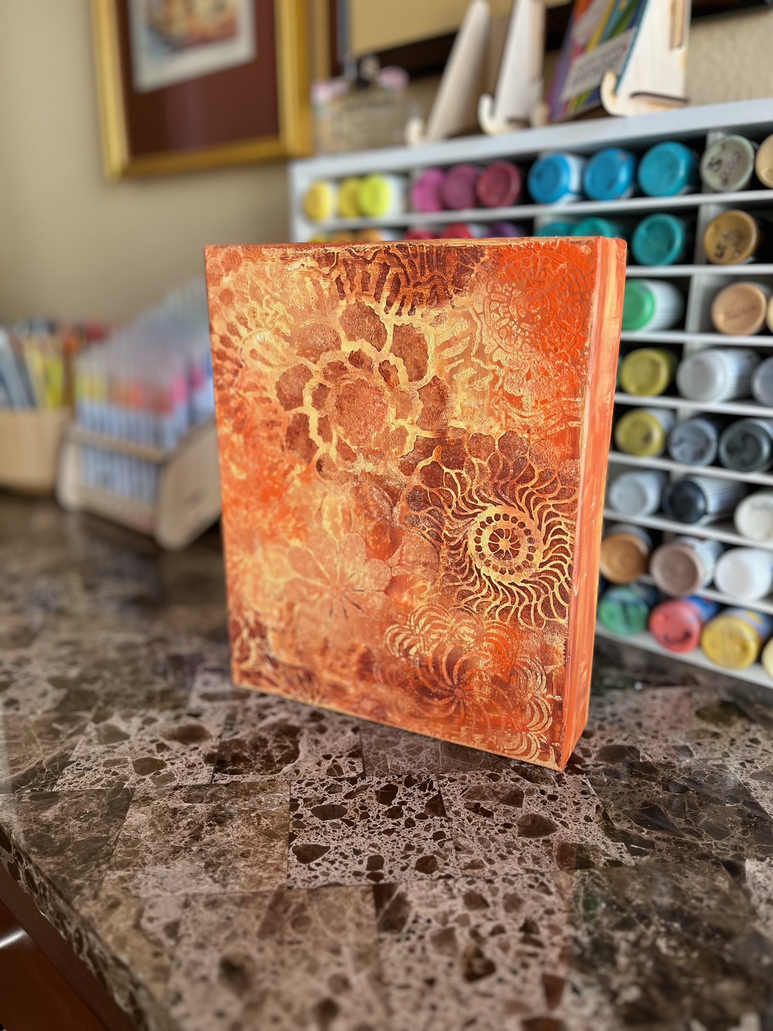 Painted puzzle box in varying shades of orange, yellow, and brown stenciled with flower patterns