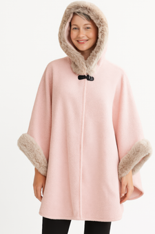 "Woman wearing a blush pink hooded cape with tan faux-fur trim on the hood and cuffs, featuring a black toggle closure at the neck."