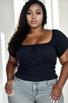 Plus-size woman wearing a black short-sleeve smocked waist top with puff sleeves and grey jeans.