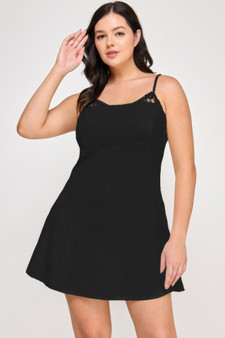 A woman wearing a short black A-line mini dress with delicate lace trim along the neckline and thin adjustable spaghetti straps.
