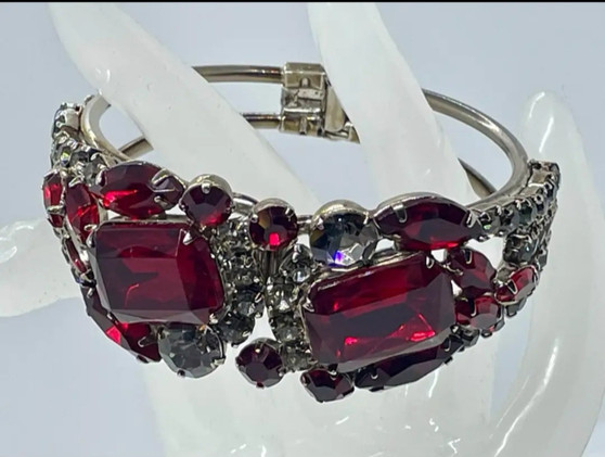 A vintage-inspired silver-tone hinged clamper bracelet showcasing oversized emerald-cut red glass cabochons and smaller chaton-shaped rhinestones in a glamorous, wide-cuff design.