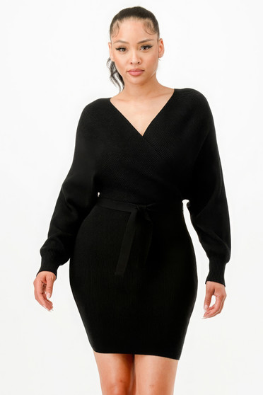 A woman wearing a black long-sleeved ribbed knit wrap dress with a V-neckline, dolman sleeves, and a matching waist tie against a plain white background.
