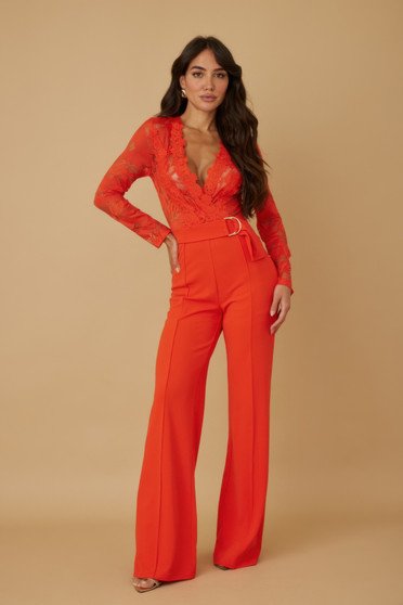 Model wearing a vibrant scarlet red jumpsuit featuring a sheer long-sleeved floral lace bodice with a scalloped V-neckline and tailored wide-leg trousers with a gold-buckle belt.