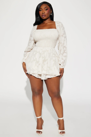 Model wearing the Everly Burnout Floral Smocked Romper in ivory. The garment features textured floral patterns, a smocked waist, and ruffled shorts that mimic a mini dress silhouette.