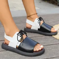 Close-up shot of a person wearing modern, black and white platform sandals. The sandals feature a wide black leather-style front band, white crisscross ankle straps with black laces, and a thick, contoured black rubber sole.