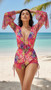 A woman standing on a tropical beach wearing a vibrant 3-piece tropical print swimsuit set featuring a sheer long-sleeve romper cover-up and matching high-waisted shorts with side ties.