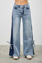 "A full-length shot of a model wearing two-tone wide-leg denim. The trousers showcase a vertical dark indigo panel running down the outer leg, ending in an adjustable tie-knot detail at the ankle."