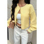 Modern street style outfit featuring a yellow cropped knit top, white leather belt, and wide-leg trousers.