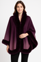 "A woman wearing a luxurious deep plum and mauve ombre cape with plush faux-fur trim along the oversized collar, sleeves, and hemline, set against a plain white background."
