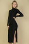 "A studio shot of a blonde model posing in a form-fitting, ankle-length black dress. The dress features a high turtleneck, long sleeves, and a textured vertical rib pattern. There is a slit on the left side reaching the mid-thigh."