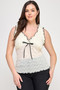 Front view of a woman wearing a cream-colored floral lace sleeveless top featuring a black ruffle trim along the V-neckline and a dainty black satin bow at the center.