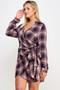 "A blonde woman wearing a plaid long-sleeve wrap dress with a deep V-neckline. The dress features a checkered pattern in shades of merlot burgundy, navy blue, and cream, with a cinched side-tie detail at the waist."