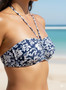 A navy blue halter bikini featuring a white flower pattern against a tropical beach background.