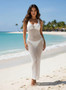"Full-length shot of a white sleeveless crochet dress featuring a grid-style knit. The dress is semi-sheer and worn as a swimsuit cover-up on a tropical beach setting."