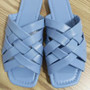 A lifestyle shot of a person wearing braided lattice-strap flat sandals with distressed skinny jeans and gold anklets.