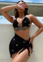 A woman wearing the Star-Struck Shimmer three-piece bikini set in sparkling black, featuring a triangle top and a matching glittery side-tie sarong wrap with ruffled edges.