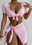A three-piece women's swim set in baby pink featuring a halter bikini top, a short-sleeve tie-front crop shrug with a bow, and a matching side-tie wrap sarong skirt. The fabric has a soft rib-knit texture.