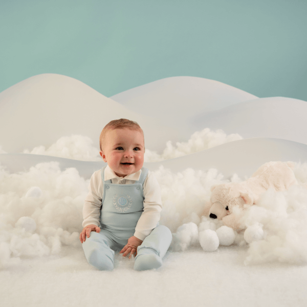 boy smiling at camera wearing a baby blue and white romper