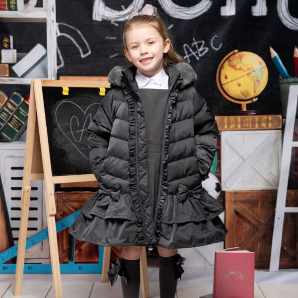 child dressed in school uniform wearing black jacket in front of multiple chalboards