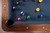 Close-up view of the walnut rail on the Doc & Holliday Preakness pool table featuring double-diamond mother-of-pearl billiard sights and a leather drop pocket.