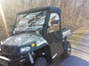 Front three-quarter view of the Side X Side cab enclosure on a camo Hisun 750 on a gravel lane in the woods