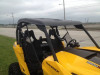 Side view of the yellow Can-Am Maverick with the Extreme Metal Products plastic top installed, parking lot behind