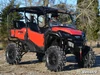 SuperATV 6-inch lift kit on a red Honda Pioneer 1000 with mud tires, front three-quarter view on gravel