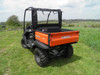 Rear three-quarter view of an orange Kubota RTV with the 3 Star soft back panel and soft top on a grassy hill