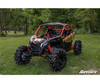 Tan and red Can-Am Maverick X3 with the SuperATV 3-inch lift kit installed in a grassy field, front three-quarter view
