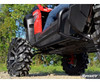 Low side view of the SuperATV nerf bar on a red CFMoto ZForce with mud tires, rider legs visible above