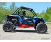 Side view of a blue Polaris RZR XP on mud tires with red SuperATV nerf bars installed, driver at the wheel