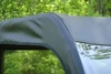 Close-up of the black 3 Star vinyl top corner and side edge seam over a Kubota utility vehicle cab, trees behind