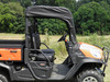 Passenger side view of the orange Kubota RTV with the 3 Star soft top and vinyl windshield, on grass