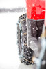 Side view of a UTV tire wrapped in Kolpin V-bar tire chains beside a red fender during snowfall