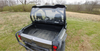 Rear three-quarter view of the 3 Star Lexan rear window on a gray Can-Am Commander in a field, cargo bed and taillights below