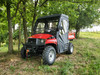 Front angle under trees of the red Coleman/Hisun 400 with 3 Star soft doors and enclosure, front bumper in view