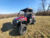 Driver side front three-quarter view of the 3 Star soft top on the red Hisun Sector 450 with trees behind
