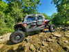 3 Star soft doors and rear window installed on a gray and orange Polaris RZR XP 4 1000 on a rocky creek bed, side view