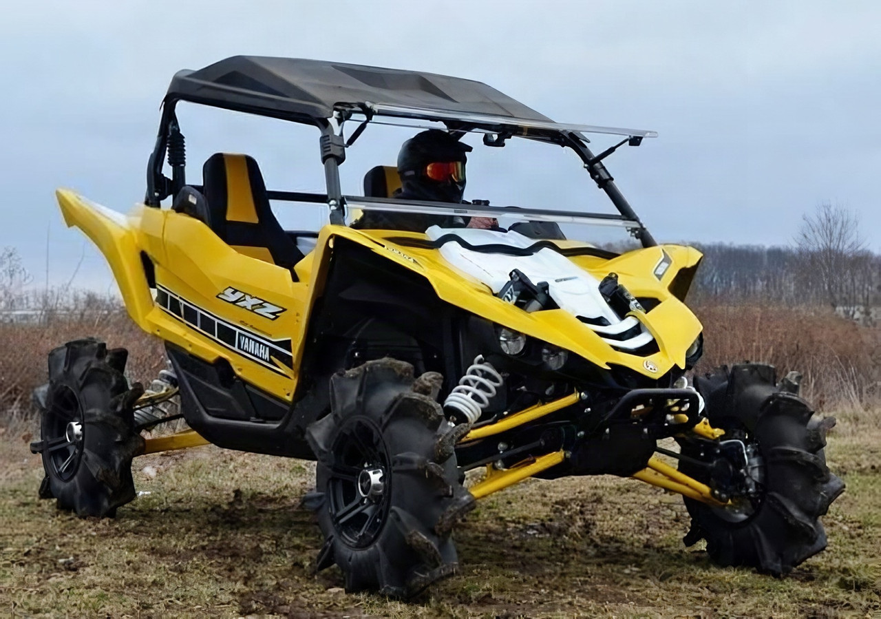 SuperATV flip out windshield installed on a yellow Yamaha YXZ with mud tires, front three-quarter view