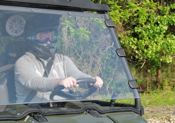 Straight-on view of the clear SuperATV windshield with the driver in goggles behind it and clamps on the Ranger cage