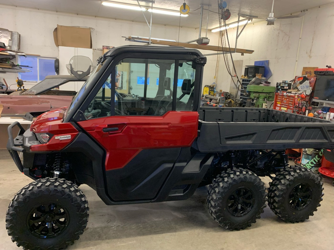 Red Can-Am Defender 6x6 with the Dirty Teeth Racing 2-inch lift installed, driver side front view in a shop