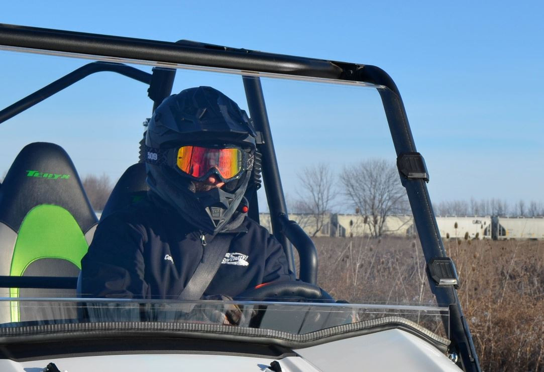 Close front view of a helmeted driver behind the SuperATV full windshield on the Kawasaki Teryx
