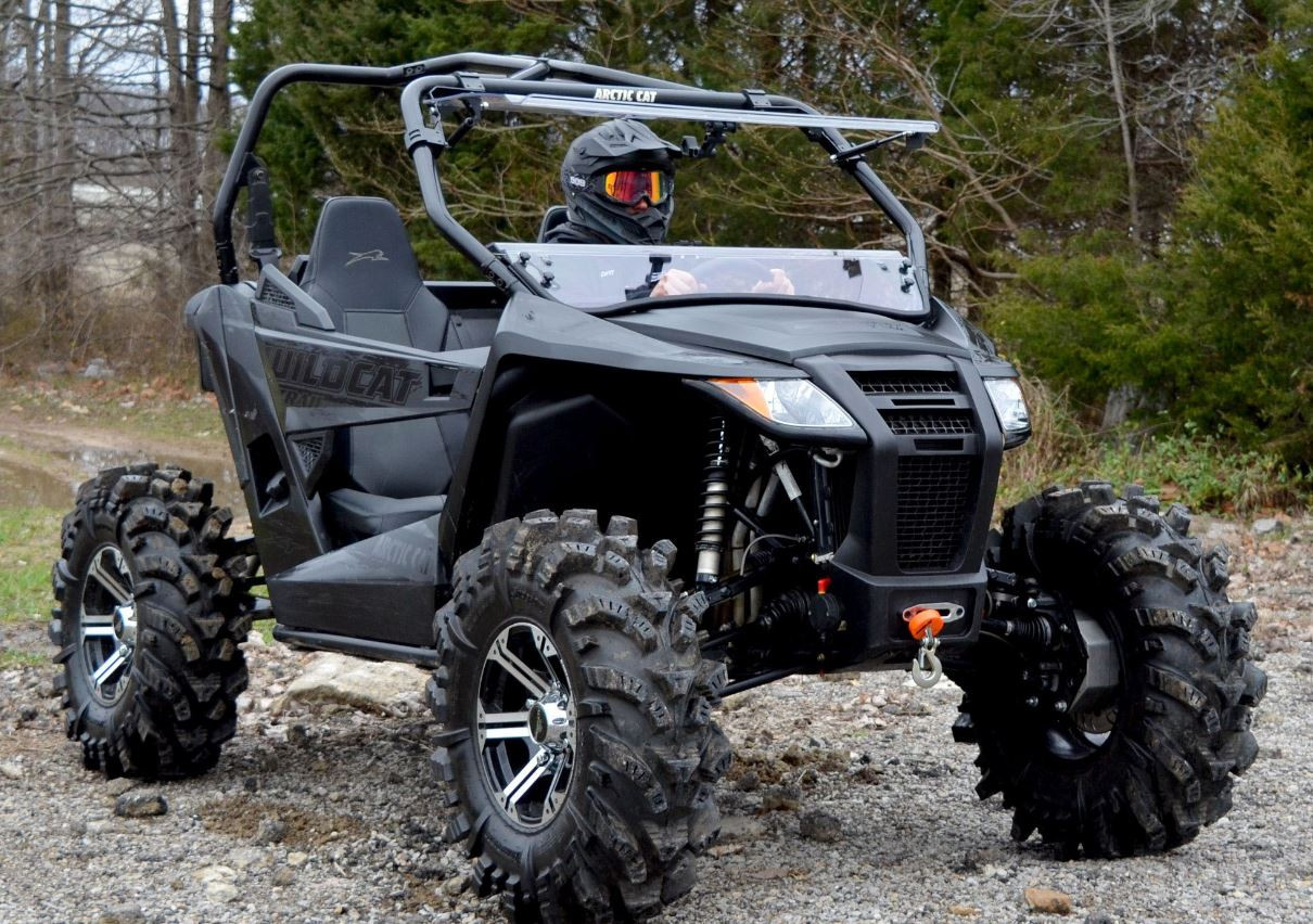 Front three-quarter view of the Arctic Cat Wildcat Trail with the SuperATV windshield top half flipped open, driver inside