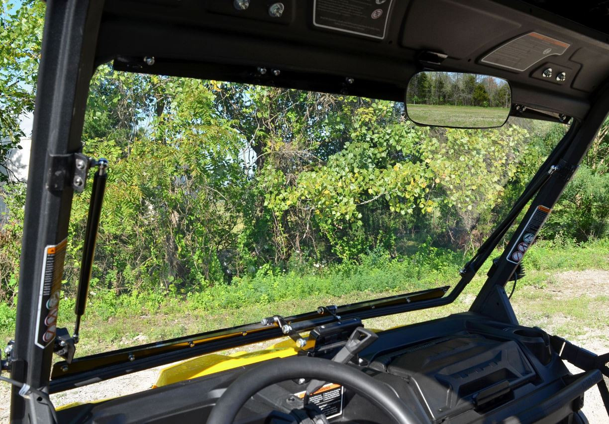 View from inside the Can Am Defender cab through the raised SuperATV windshield showing the gas strut and mirror