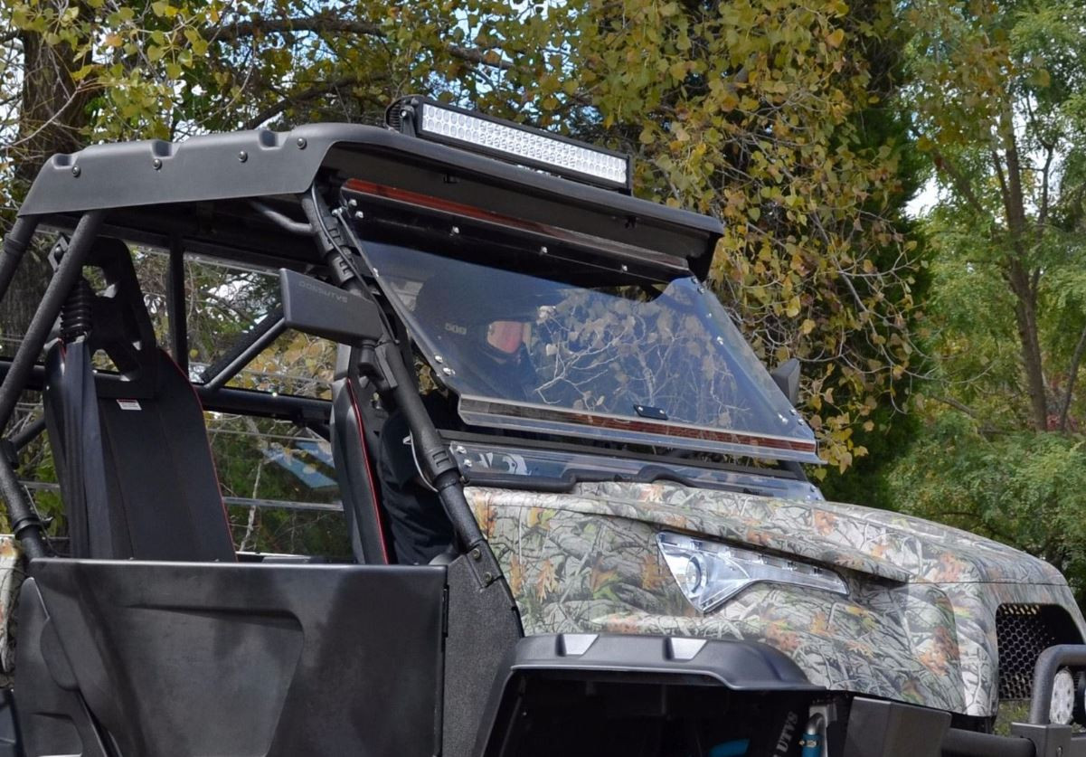 Camo Odes Dominator with the SuperATV flip-up windshield closed, passenger side three-quarter view among trees