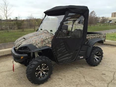 Front three-quarter view of a camo Massimo side-by-side wearing the Side X Side over-roof cab enclosure with clear windshield