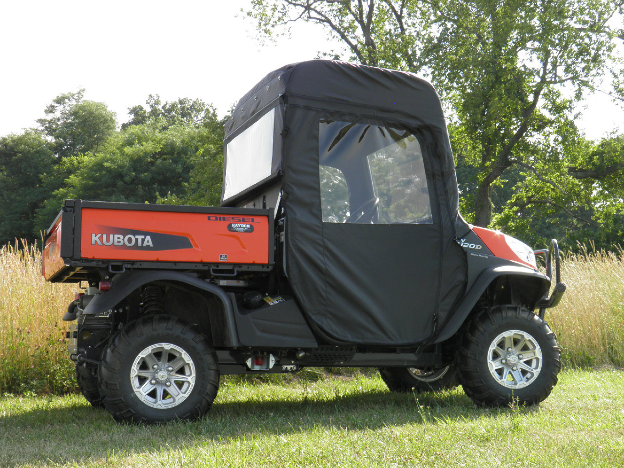 3 Star full cab enclosure installed on an orange Kubota RTV, black soft cab with clear windows, side view in a field